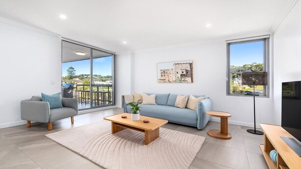 A modern living room with a grey sofa, a blue sofa, a wooden coffee table, and a floor lamp. There is a large window with a view of a residential area. - Oceans Edge #25 | Top Floor,1 Min to Terrigal Beach| Accom Holidays (TERRIGAL)