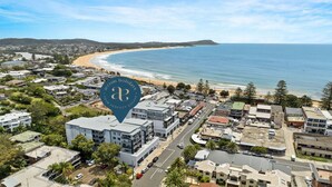 An aerial view of a coastal town with a beachfront, residential buildings, and a prominent hotel sign. - Oceans Edge #25 | Top Floor,1 Min to Terrigal Beach| Accom Holidays (TERRIGAL)