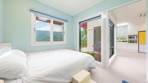 A bedroom with a large bed, a window with a view of greenery, and a kitchen area visible through an open door. - Gyeongsan Stage-ipple pet Pension (Gyeongsan)