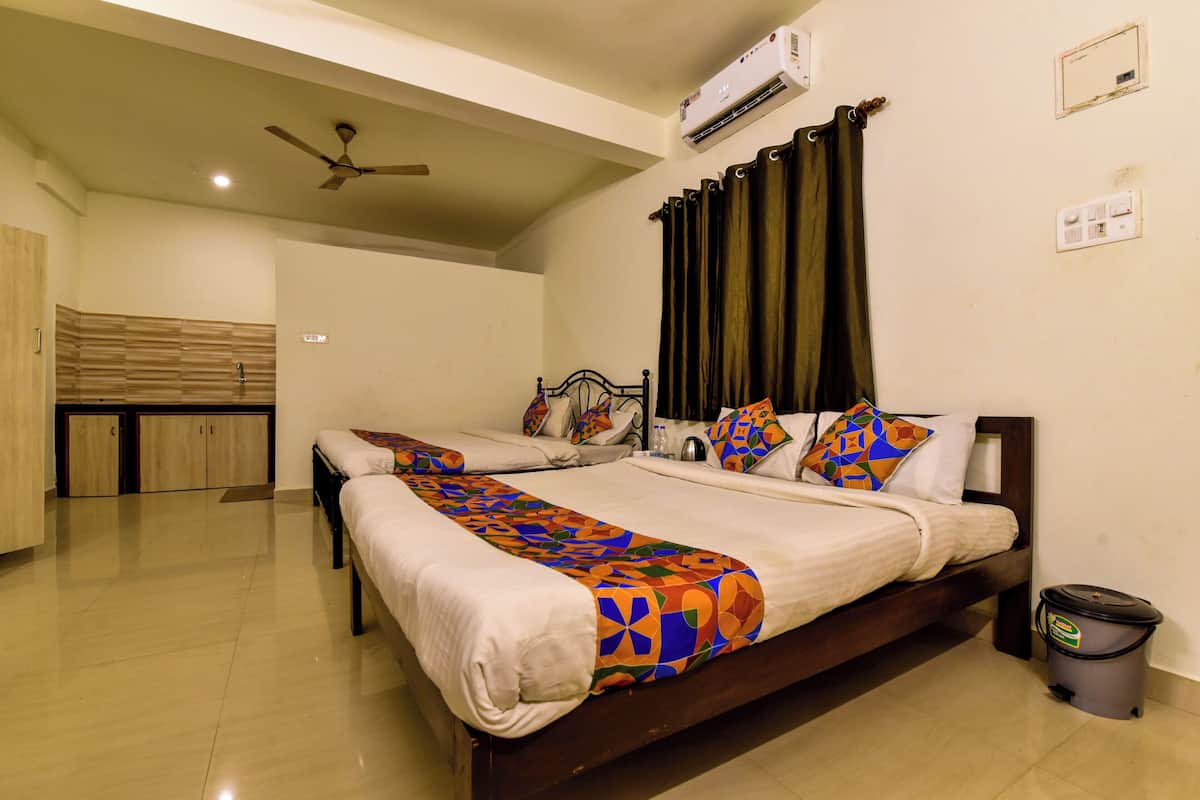 A hotel room with two beds, a ceiling fan, an air conditioning unit, a bathroom with a toilet, and a trash bin.