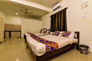 A hotel room with two beds, a ceiling fan, an air conditioning unit, a bathroom with a toilet, and a trash bin. - Rosa Bella Resort (Calangute)