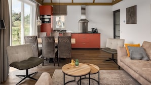 A modern living room with a sofa, chairs, a dining table, and a kitchen in the background. - Villa in Someren Near Somerense Heide (Someren)