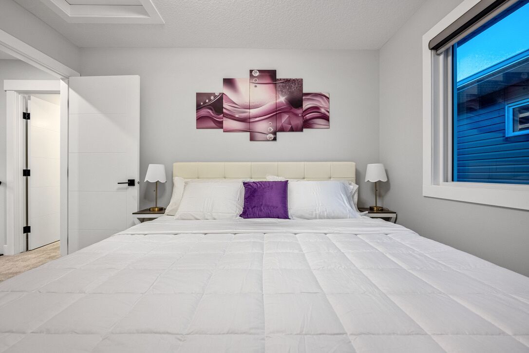 A modern bedroom with a large bed, a headboard, bedside lamps, and a wall art piece.