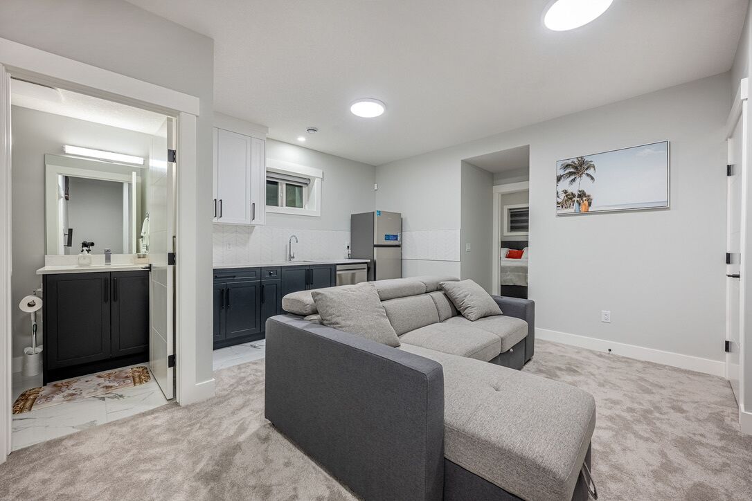 A modern apartment with a grey sofa, a kitchen with dark cabinets, and a small dining area.