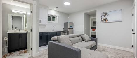 A modern apartment with a grey sofa, a kitchen with dark cabinets, and a small dining area.
