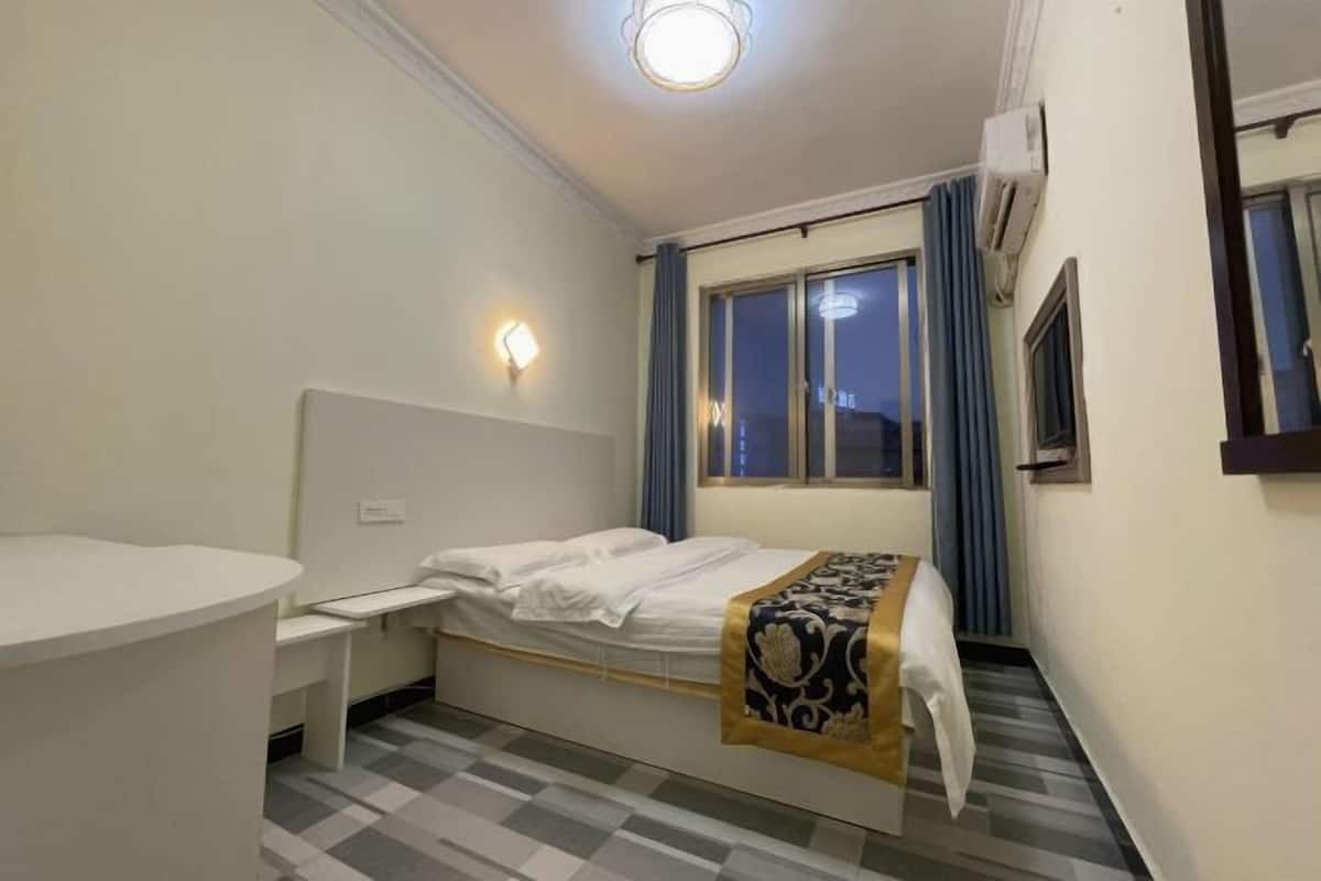 A hotel room with a bed, bedside table, and a window with curtains.