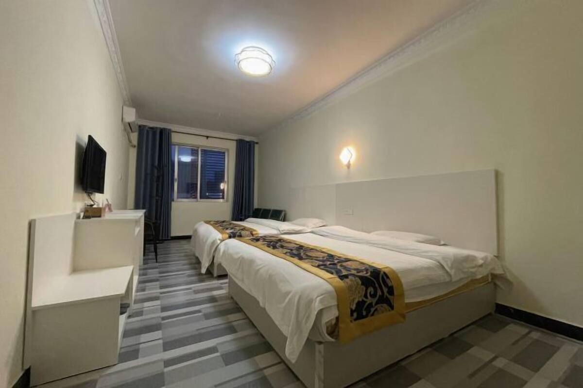 A hotel room with two beds, a desk, a TV, and a window with curtains.