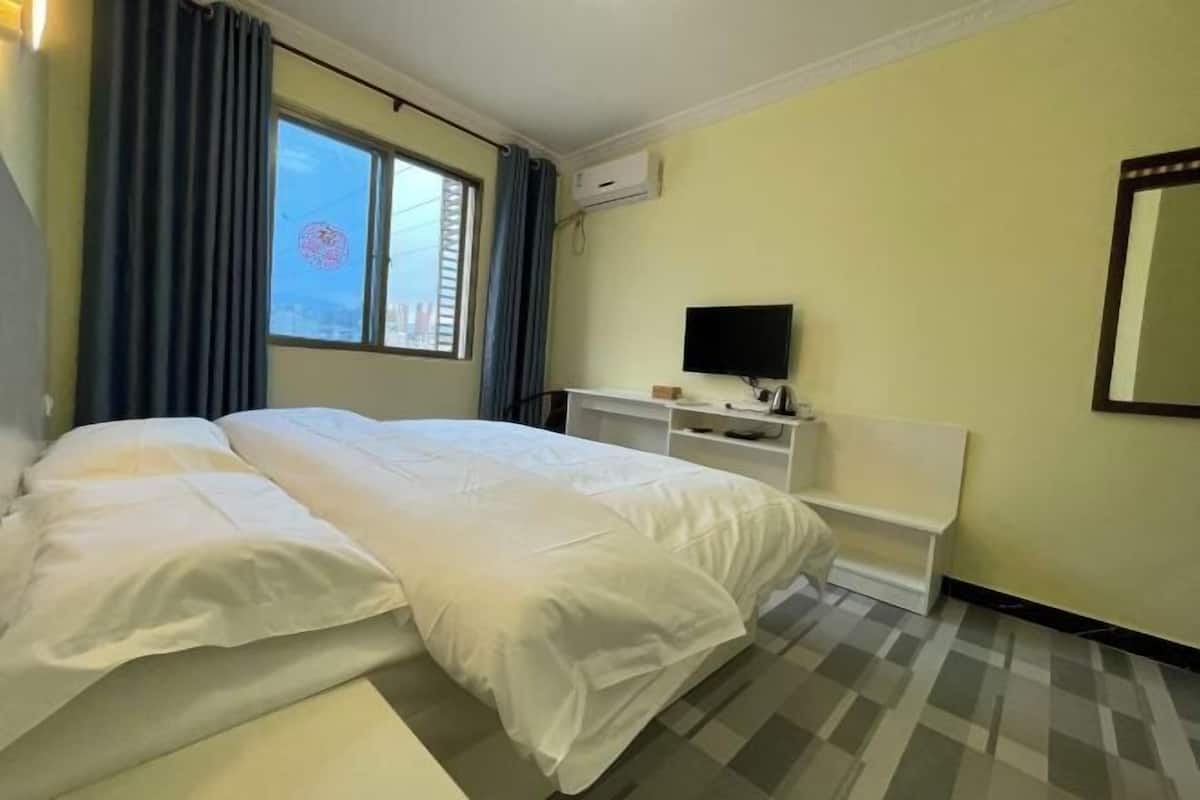 A hotel room with a bed, a TV, a desk, and a window with curtains.