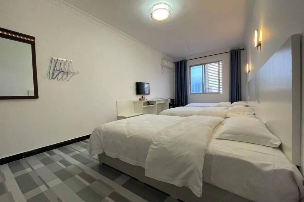 A hotel room with two beds, a TV, a mirror, and a window with curtains.