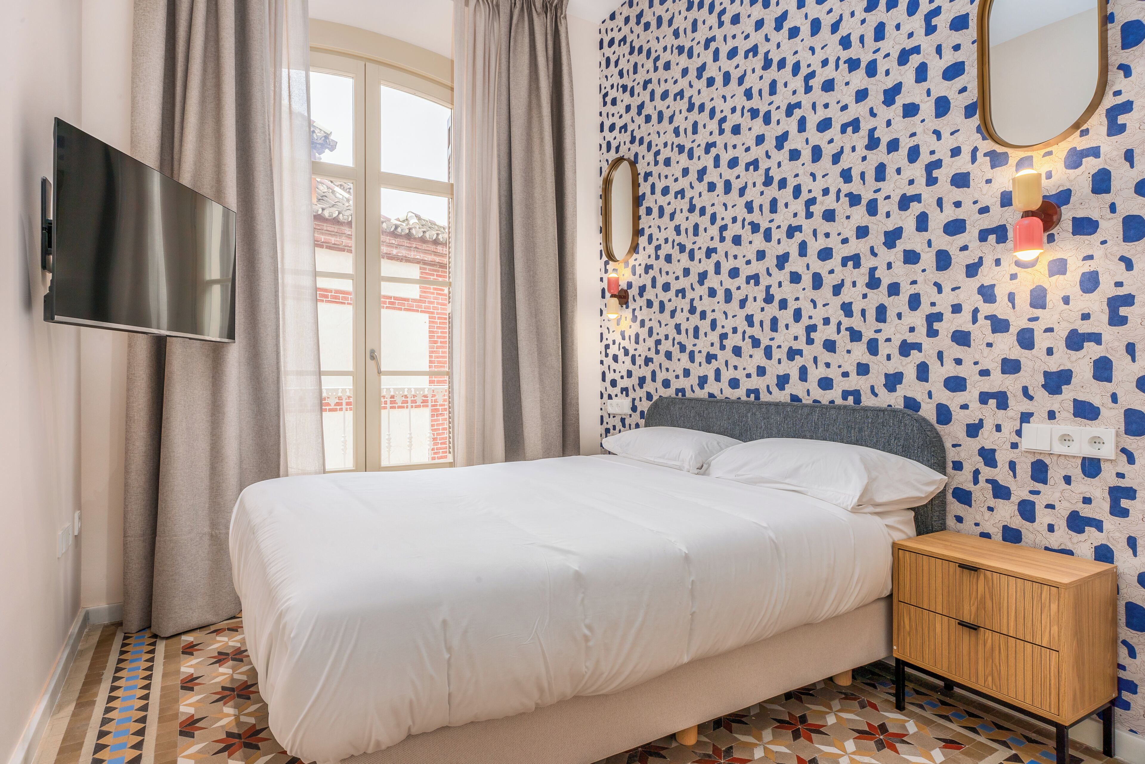 Ein Schlafzimmer mit einem Bett, einem Fernseher, einem Nachttisch und einer Wand mit Muster.