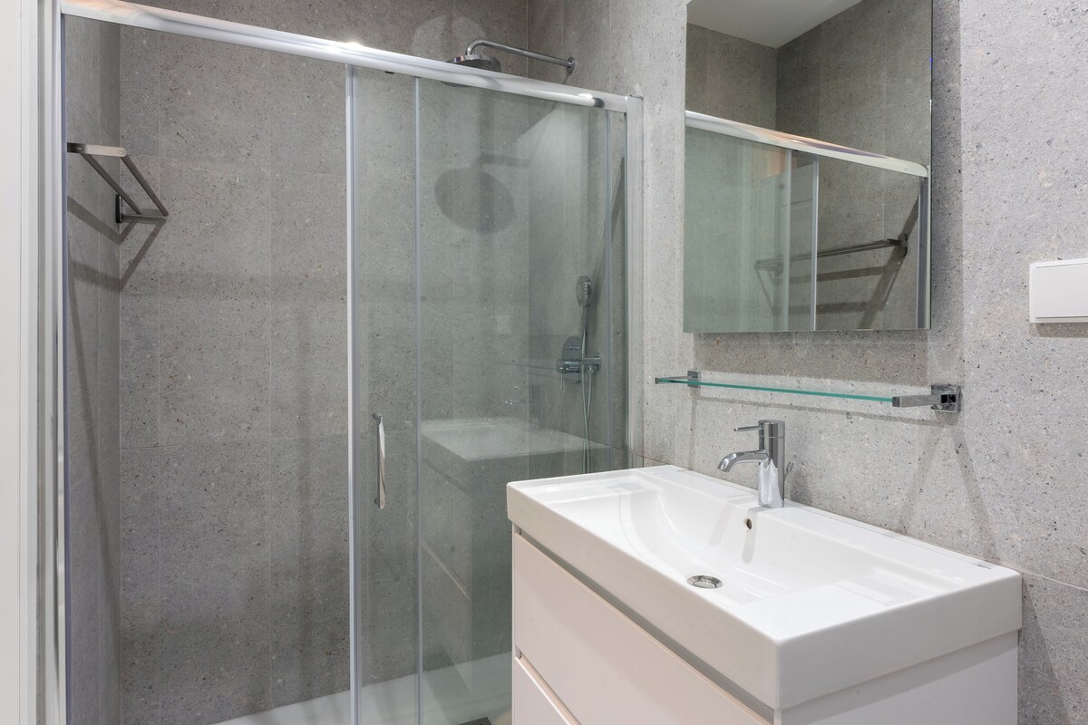 A modern bathroom with a glass shower enclosure, a white sink, and a mirror above it.