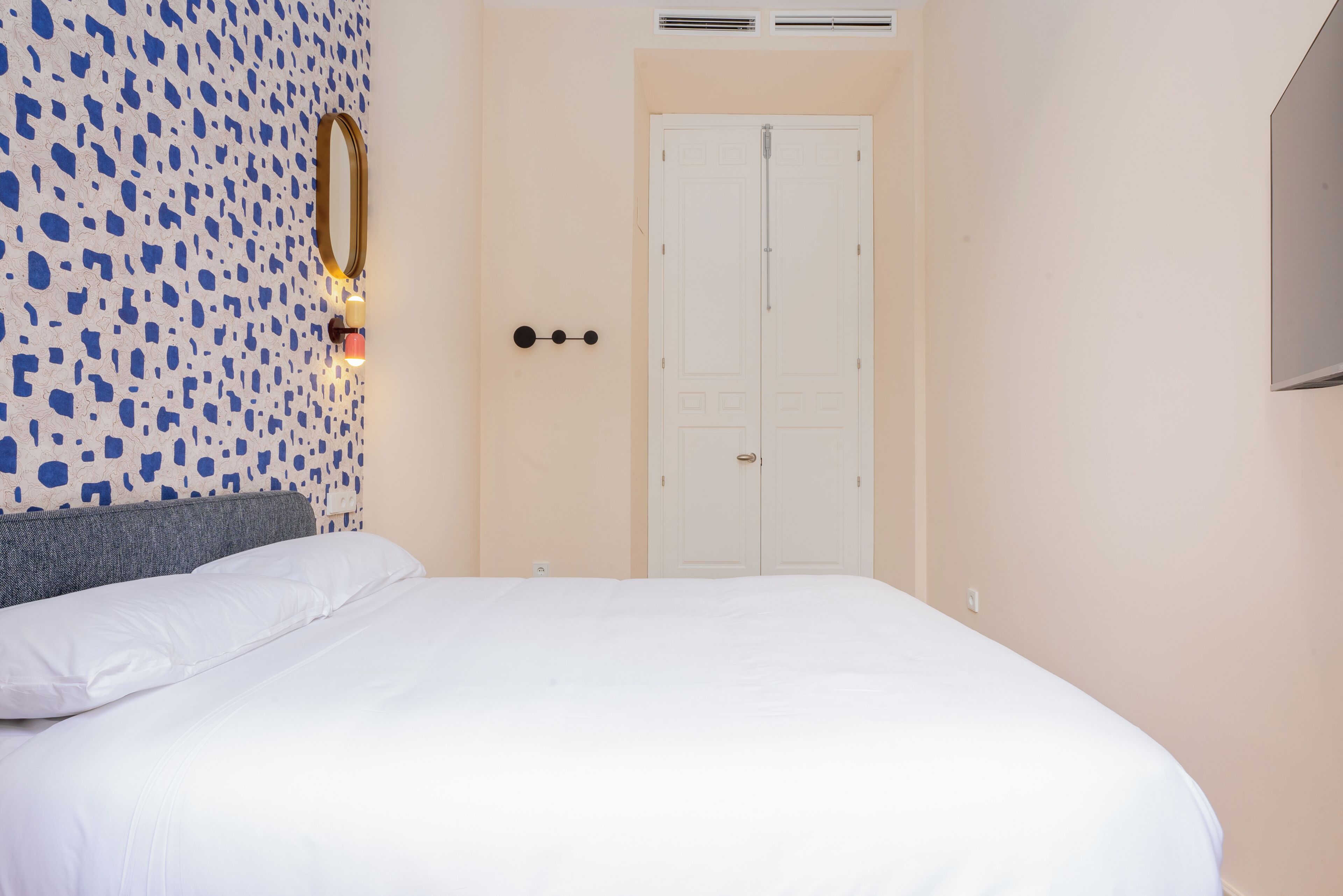 Un dormitorio con una cama, un espejo en la pared, una lámpara y una puerta.