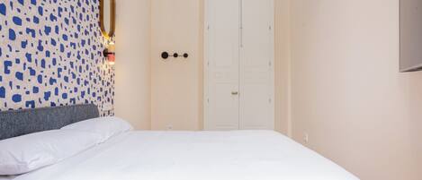 Un dormitorio con una cama, un espejo en la pared, una lámpara y una puerta.