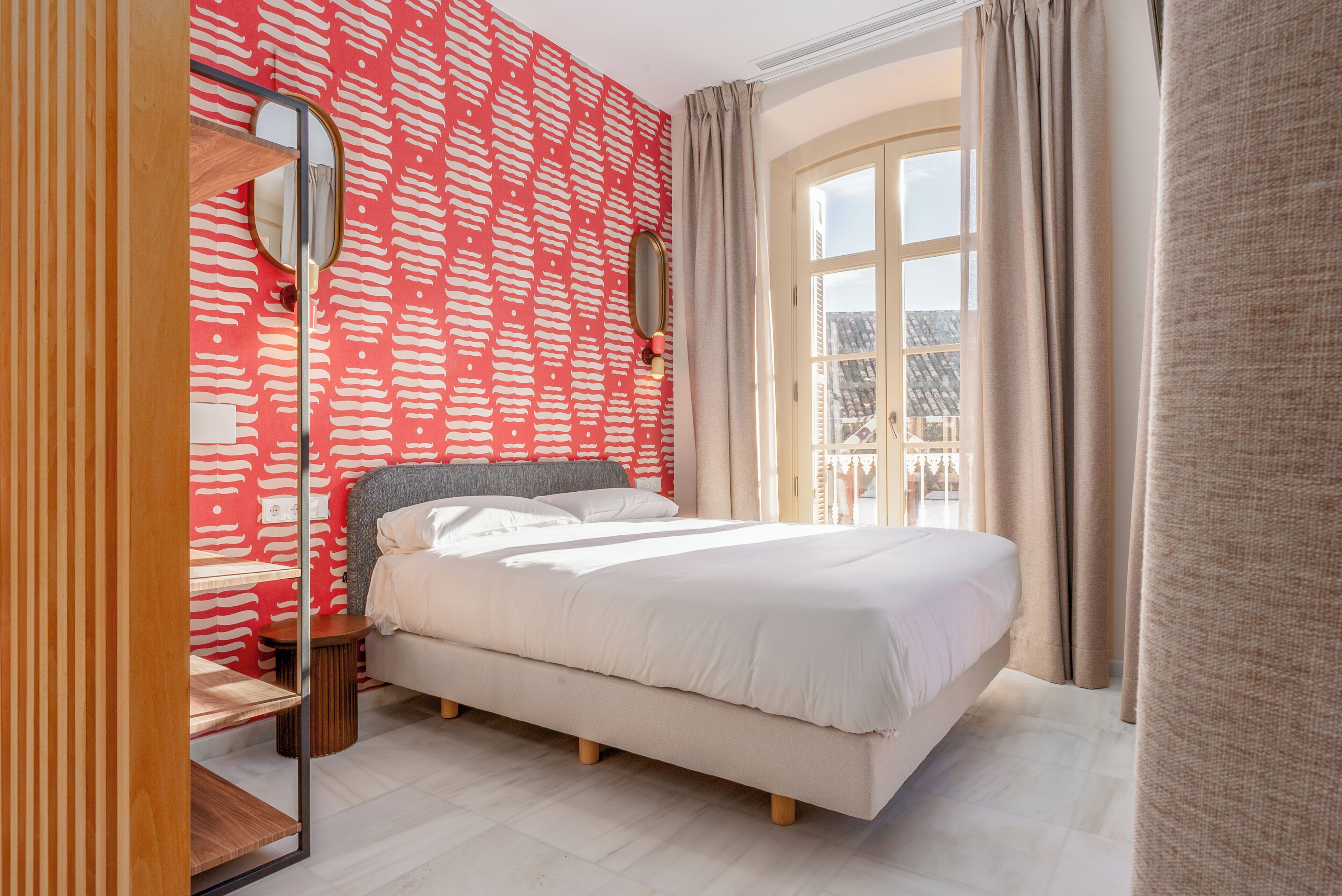 Un dormitorio con una cama grande, un espejo, una mesita de noche de madera y una ventana con cortinas.