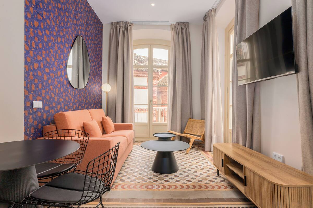 Una sala de estar moderna con un sofá, una mesa redonda de centro, un televisor montado en la pared y un tapete estampado.