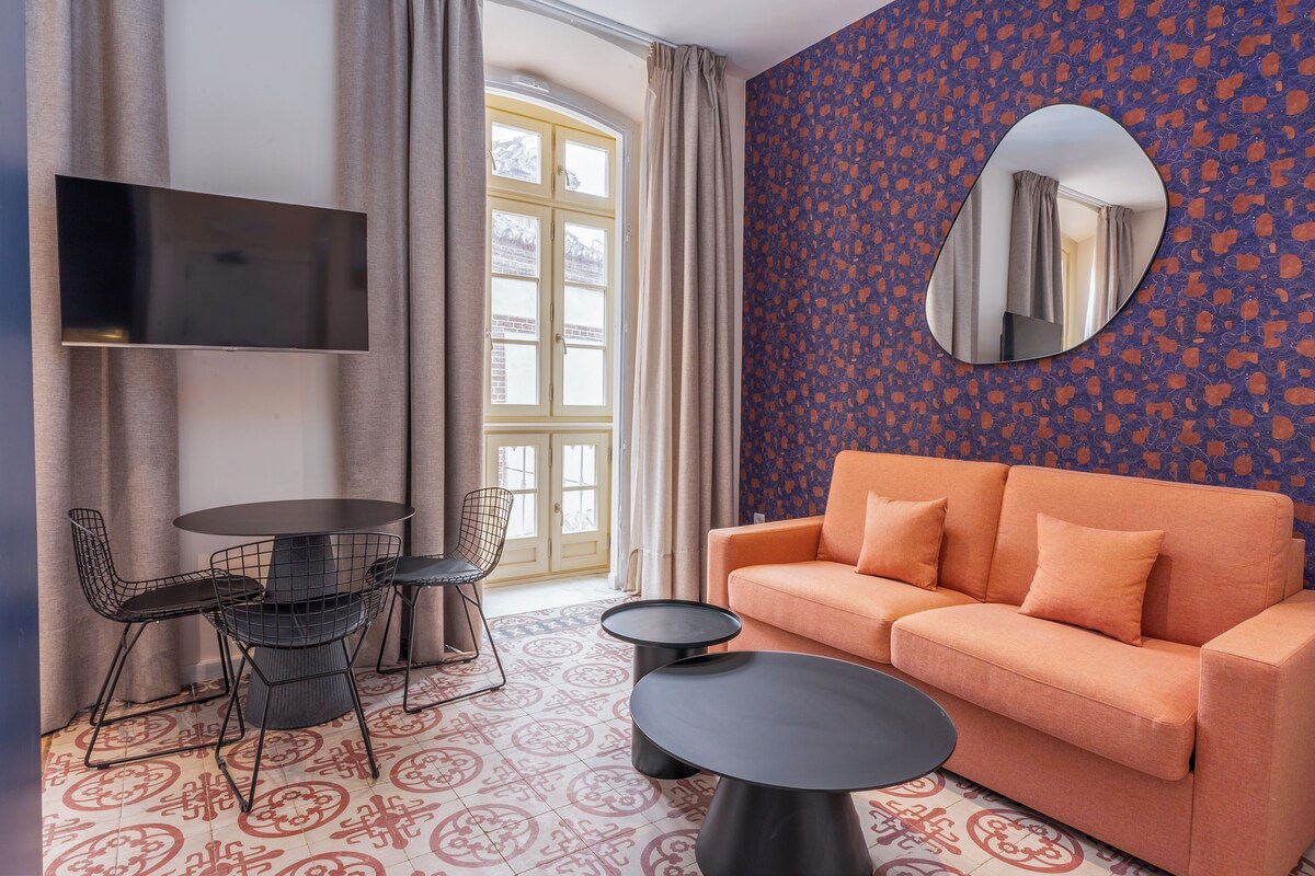 A modern living room with a sofa, a TV, a round table, and a patterned floor.