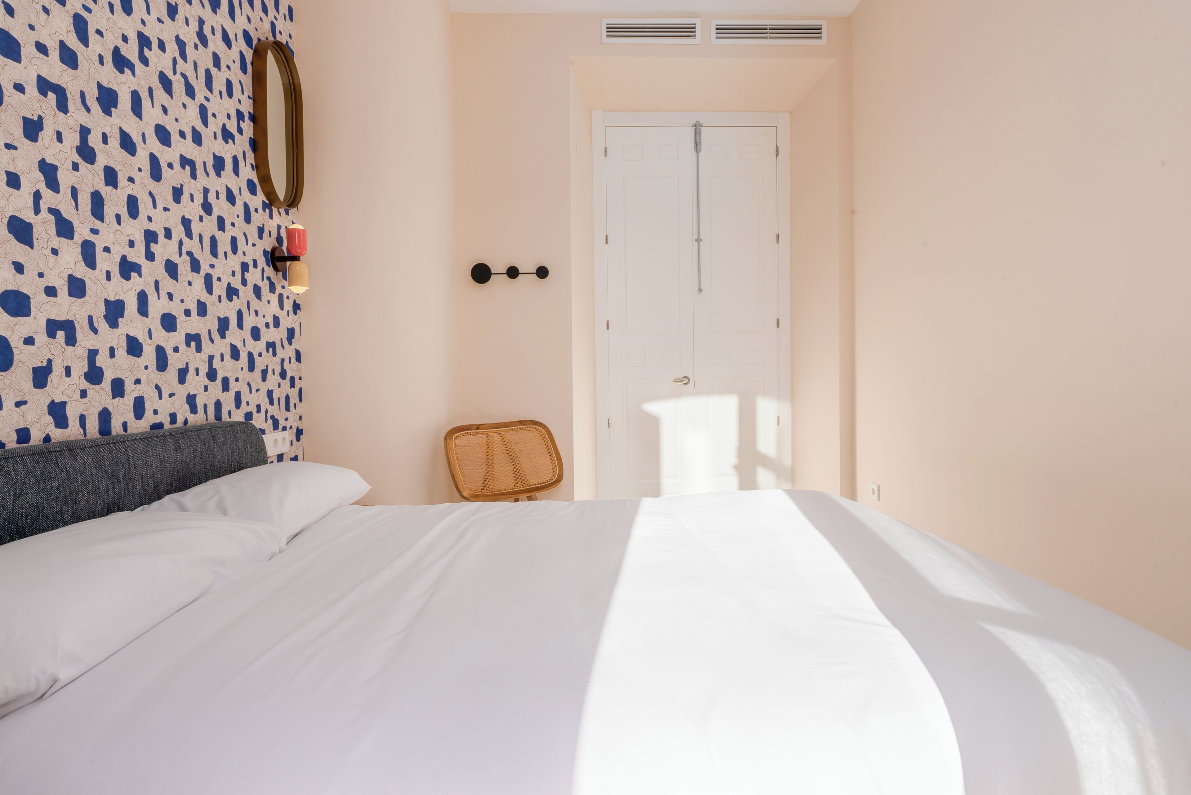 A hotel room with a bed, a chair, a mirror, and a door.