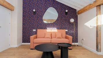 Una sala de estar moderna con una pared estampada, un sofá, dos mesas negras y un espejo grande.