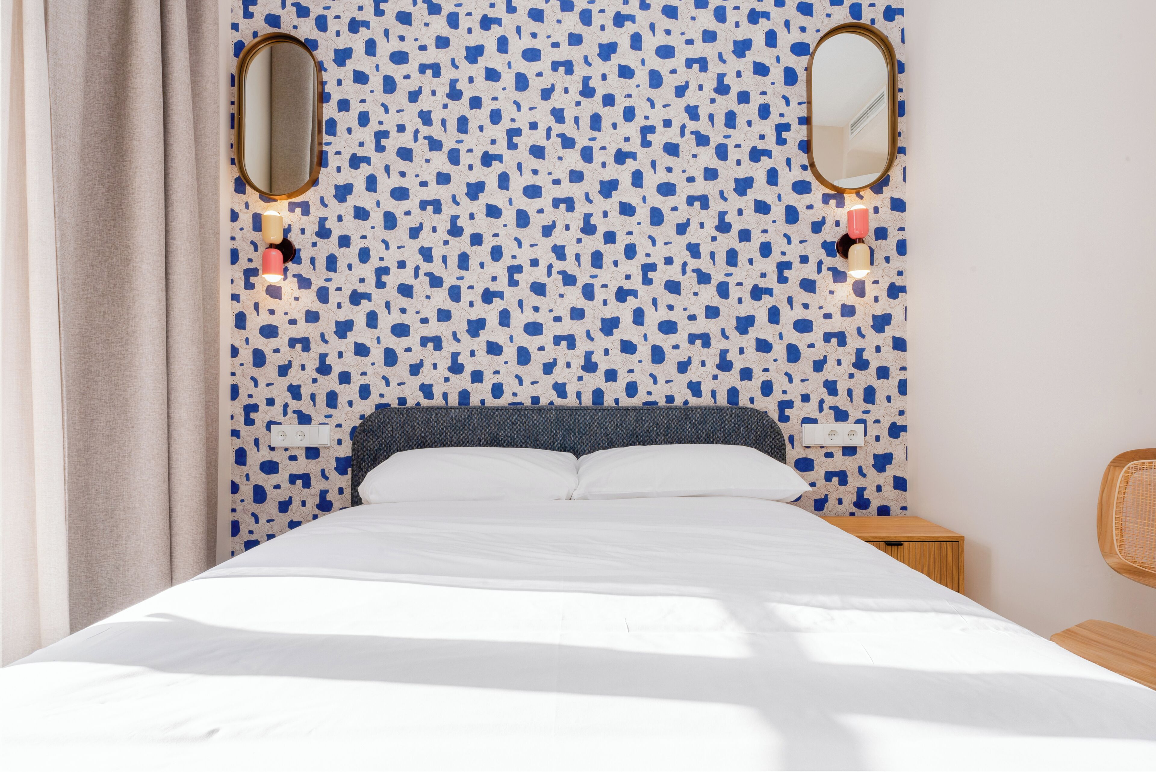 Una cama con ropa de cama blanca, una pared con salpicaduras azules y blancas, y dos espejos encima.
