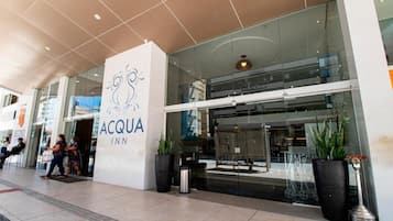 The exterior of the ACQUA INN, featuring a modern glass facade, a prominent logo, and potted plants.