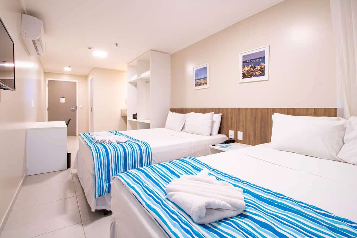 Habitación de hotel con dos camas, un escritorio, una silla, un armario y baño.