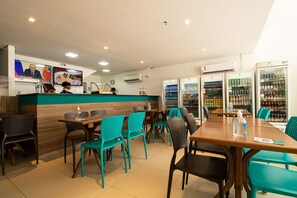 A restaurant interior with teal chairs, wooden tables, a counter with a menu, and beverage refrigerators. - Acqua Inn Maceio Ponta Verde (Maceió)