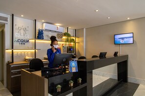 Mostrador de recepción de hotel con computadora, monitor y un cartel que indica un programa de fidelización.