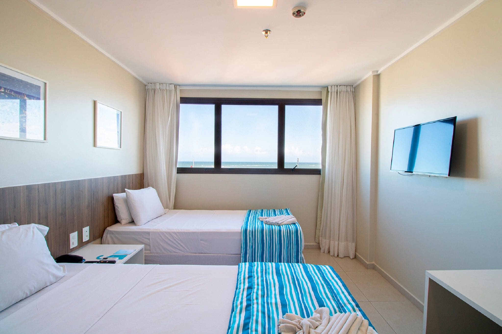 Habitación de hotel con dos camas, televisión y ventana con vista al mar.
