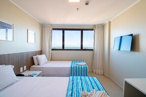 Habitación de hotel con dos camas, televisión y ventana con vista al mar.