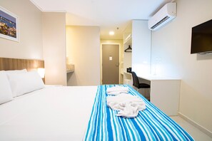 Una habitación de hotel con cama, escritorio, silla, televisor y aire acondicionado.