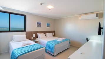 A hotel room with two beds, a desk, and a view of the sea.
