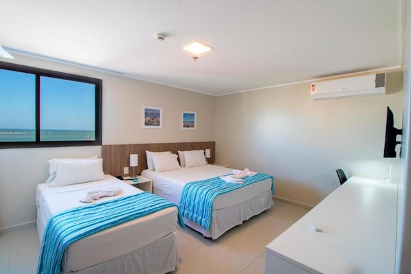 Habitación de hotel con dos camas, un escritorio y vista al mar.