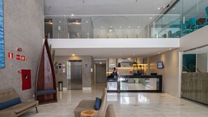 A modern lobby with a reception desk, seating area, and a staircase leading to an upper level. - Acqua Inn Maceio Ponta Verde (Maceió)