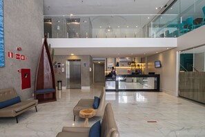 Un lobby moderno con una recepción, un área de estar y una escalera que sube a un nivel superior.