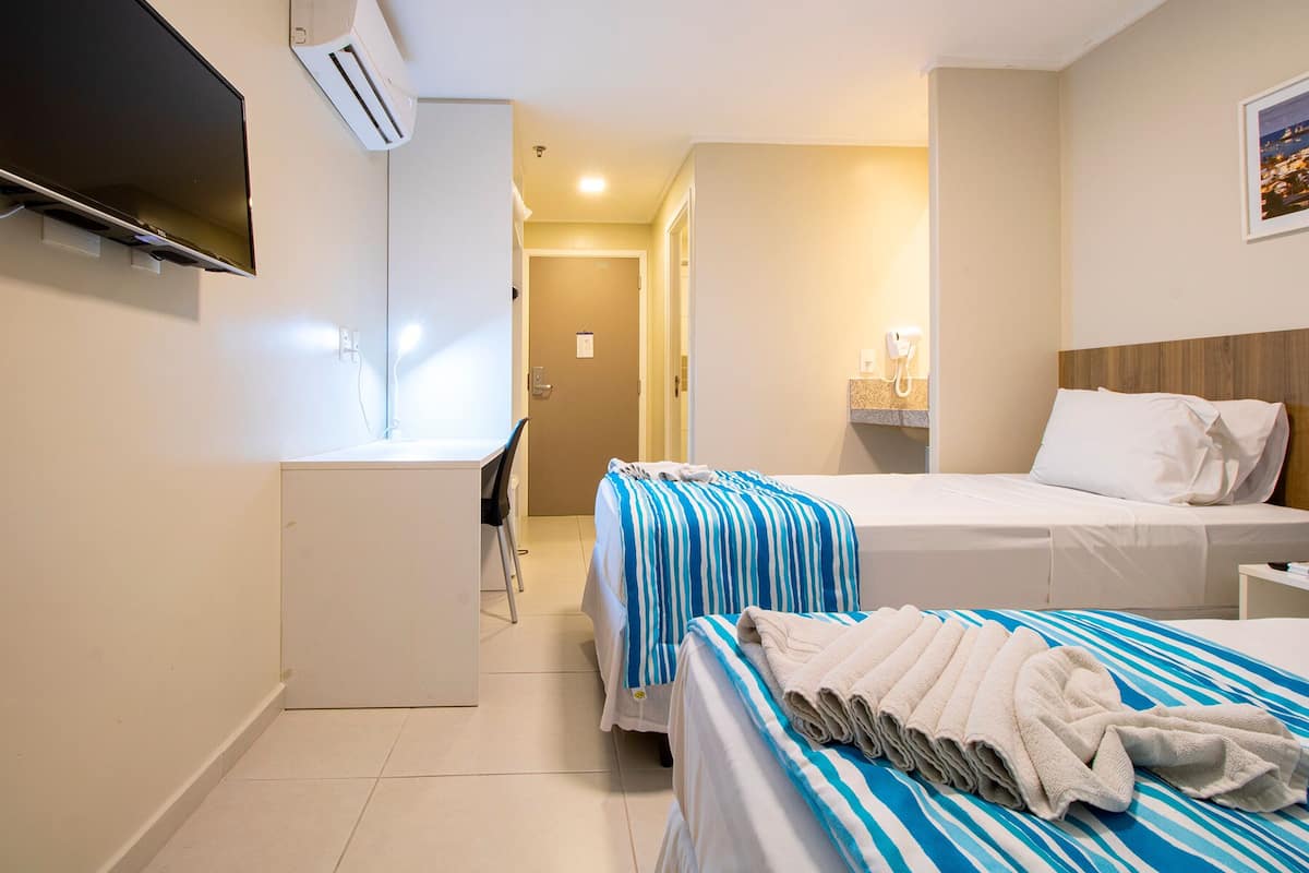 Una habitación de hotel con escritorio, cama con ropa de cama a rayas, televisor y aire acondicionado.