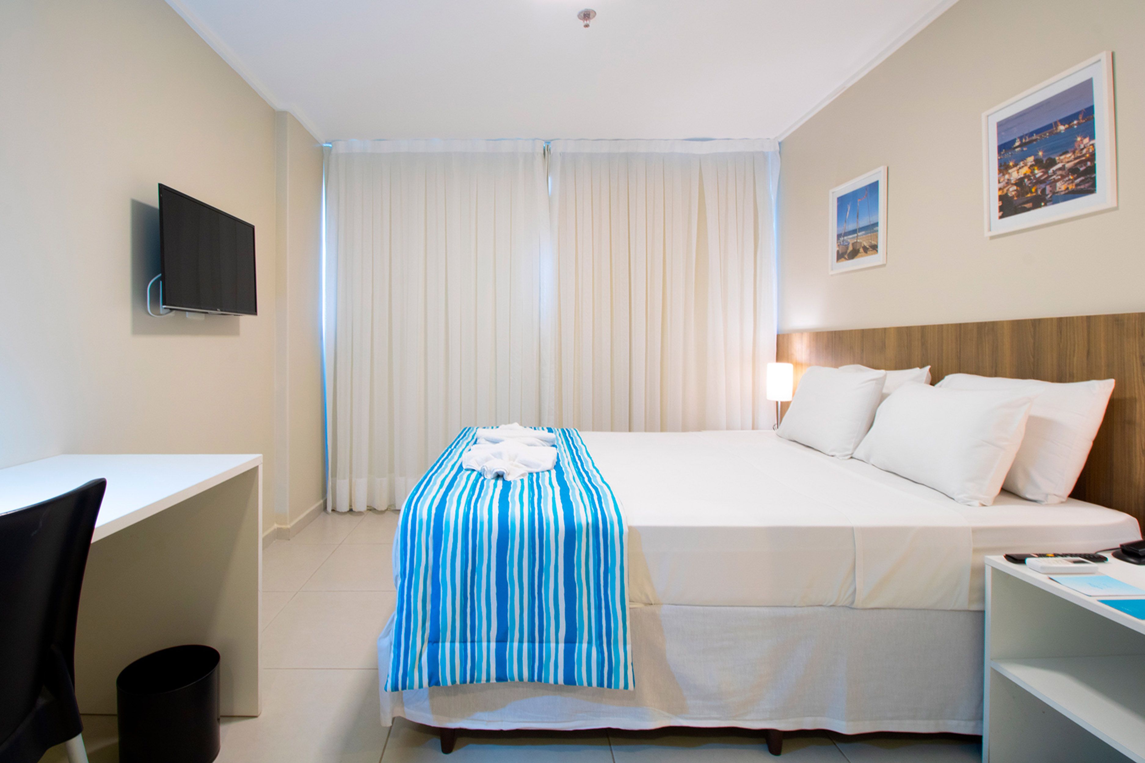 A hotel room with a bed, a desk, a chair, a TV, and a window with curtains.