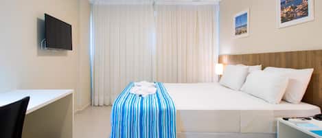 A hotel room with a bed, a desk, a chair, a TV, and a window with curtains.