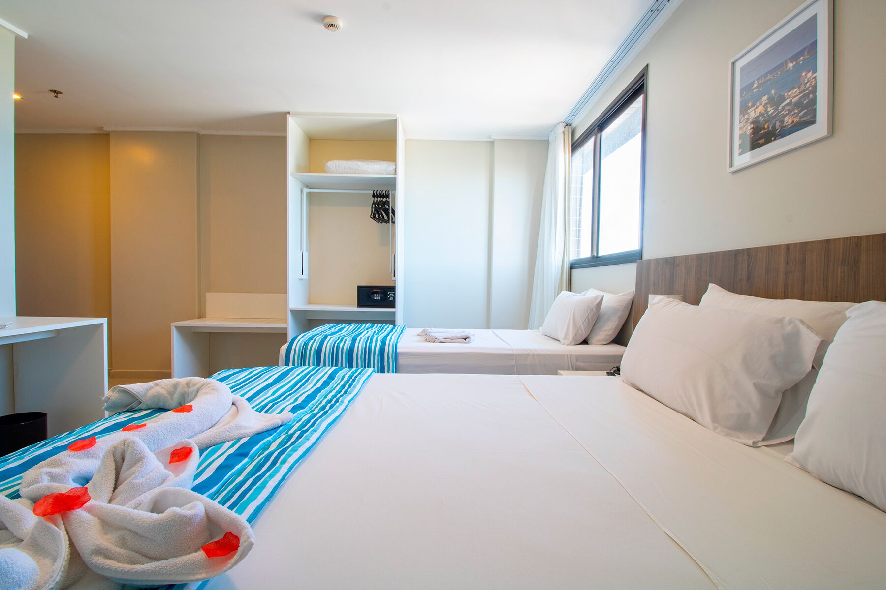 Habitación de hotel con dos camas, un escritorio, un armario y ventana con vistas a la ciudad.