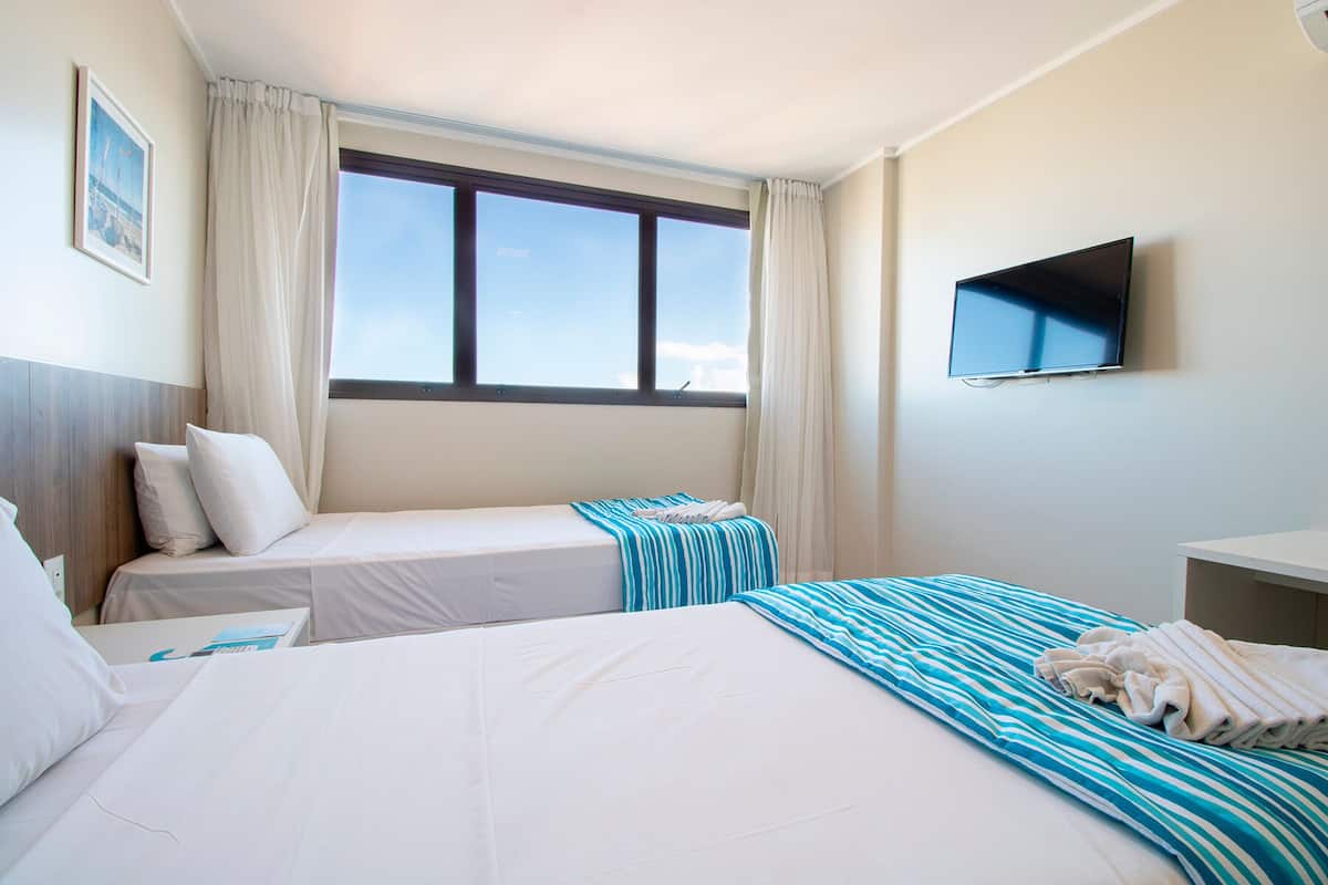 Habitación de hotel con dos camas, televisión y ventana con cortinas.