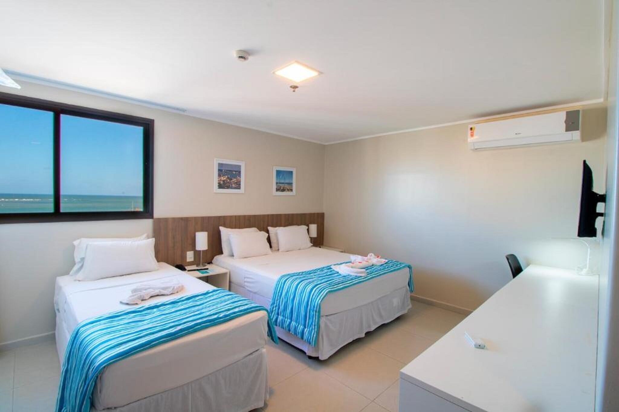 Habitación de hotel con dos camas, un escritorio y vista al mar.