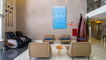 A lobby with massage chairs, a wooden table, and a large painting of water.