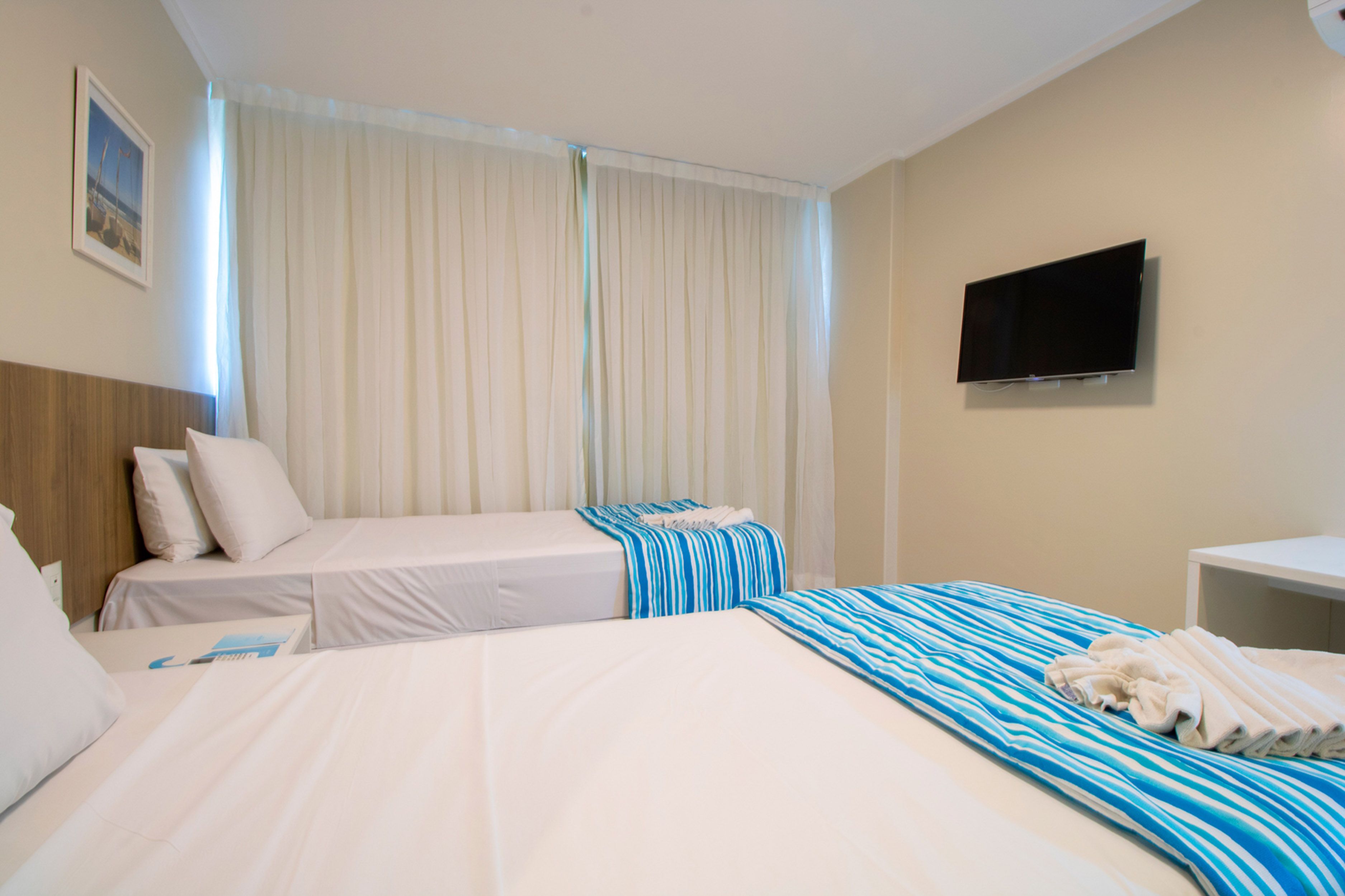 A hotel room with two beds, a TV, and a window with curtains.