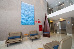 A lobby with two leather sofas, a large abstract painting, a red emergency exit sign, and an elevator. - Acqua Inn Maceio Ponta Verde (Maceió)
