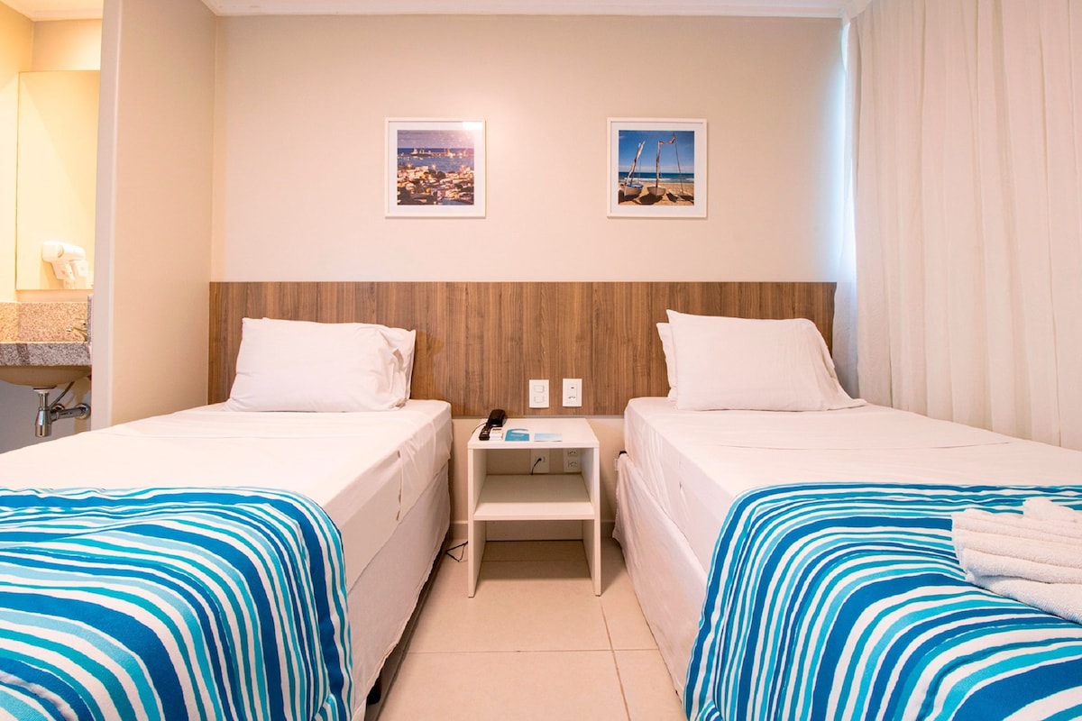 A hotel room with two beds, a nightstand, and a bathroom visible.