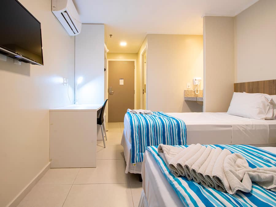 Una habitación de hotel con dos camas, un escritorio, un televisor y un aire acondicionado.