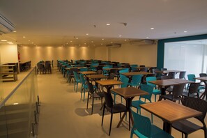 Un salón de conferencias con filas de mesas y sillas, una división de vidrio y una pizarra en la pared.