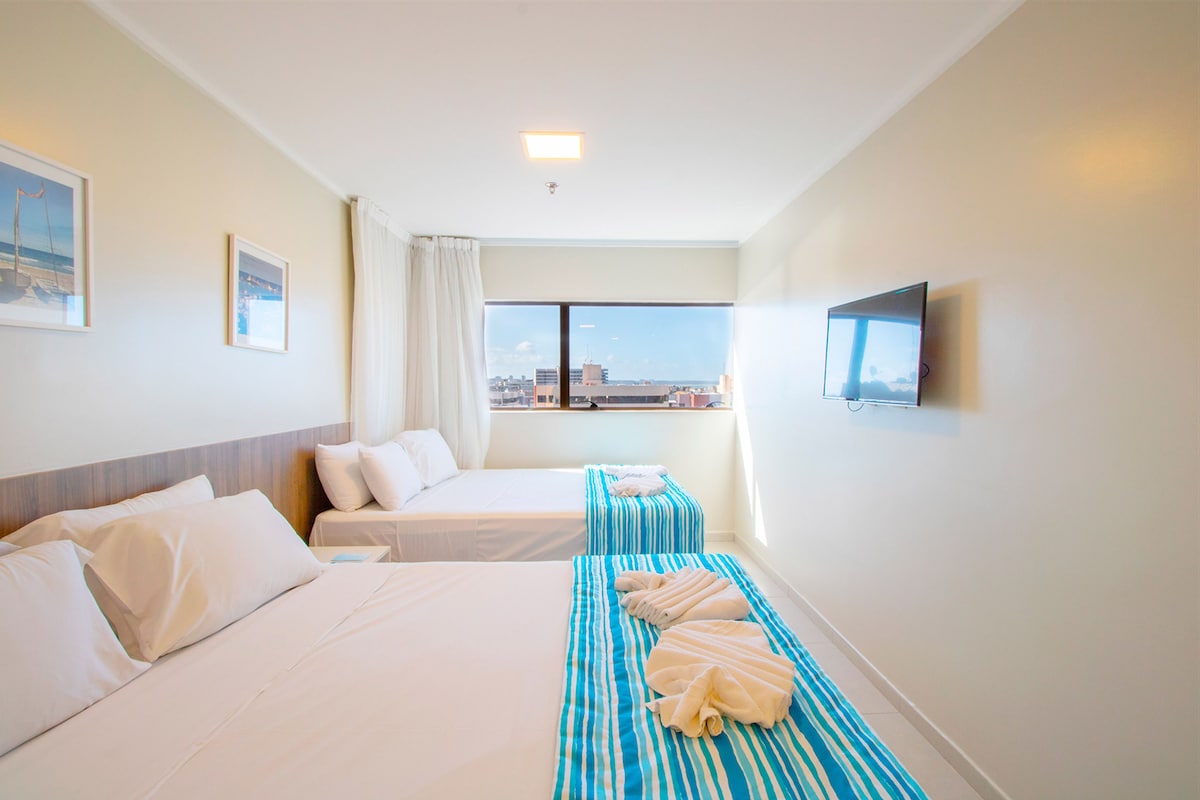 A hotel room with two beds, a TV, and a window with a city view.