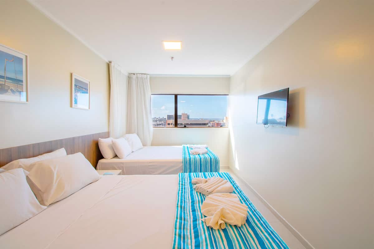 A hotel room with two beds, a TV, and a window with a city view.