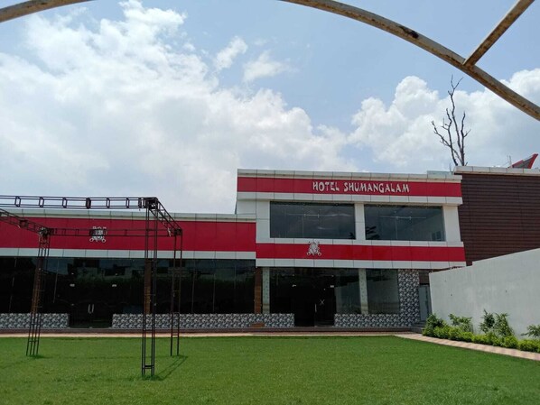 A modern hotel with a red and white facade, large windows, and a well-maintained lawn.