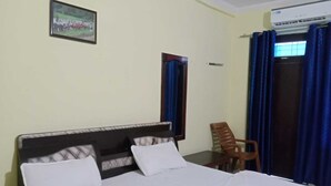 Ett hotellrum med en säng, en stol, ett fönster med gardiner och en väggmonterad luftkonditioneringsanläggning.